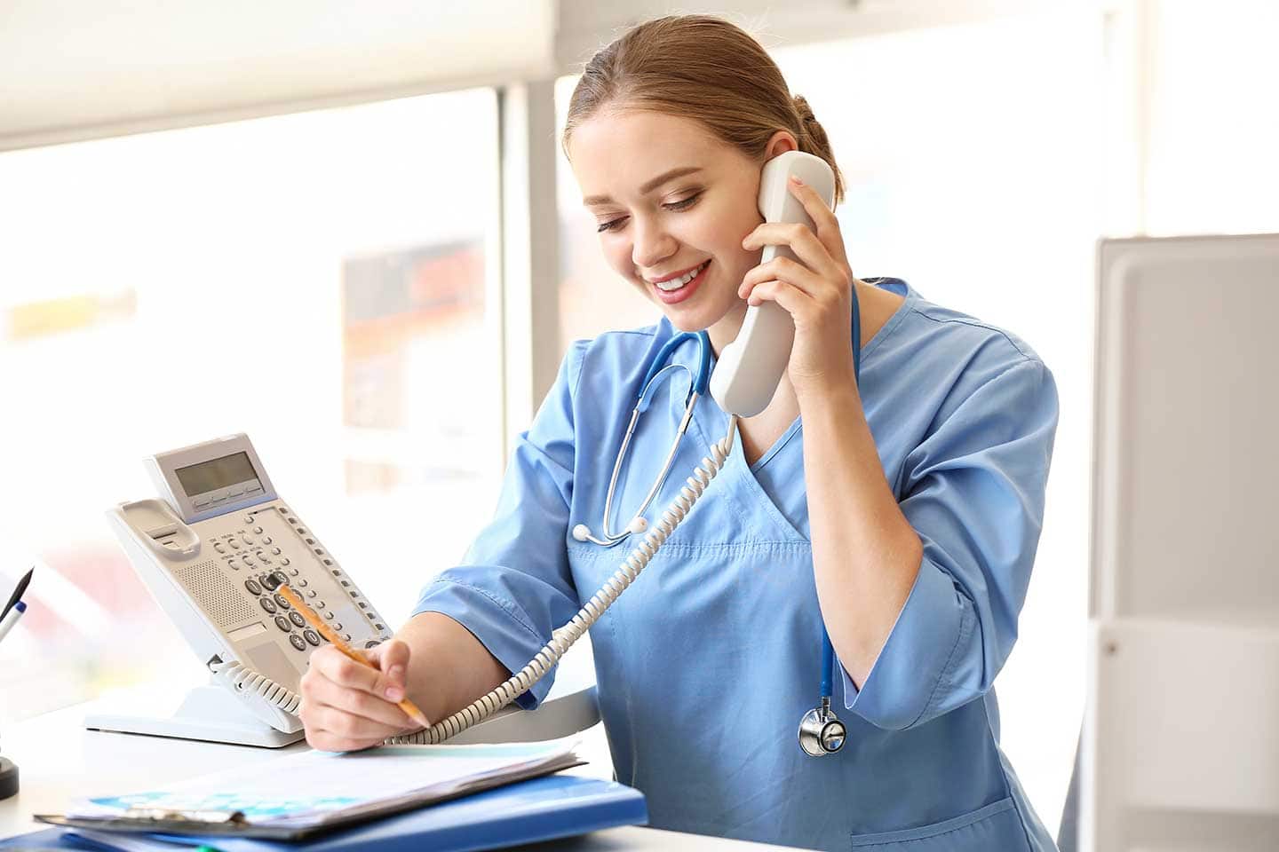 Medizinische Fachangestellte in einer Arztpraxis, die telefoniert und sich Notizen macht.